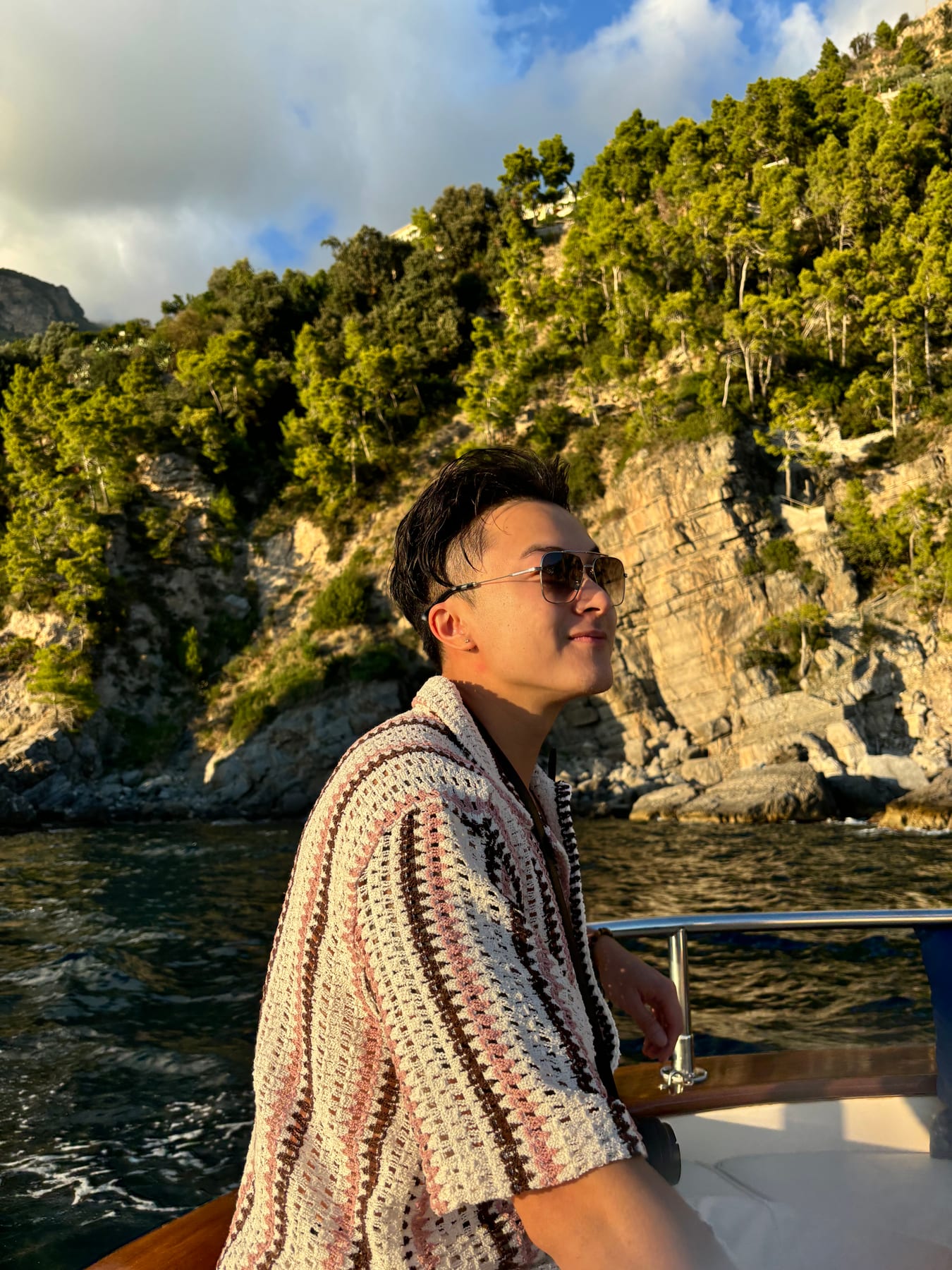 John Wen on a boat along a tree-lined rocky coast